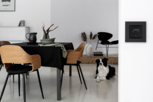 Polski system inteligentnego domu SIMON GO – czarny termostat na ścianie w nowoczesnym wnętrzu.