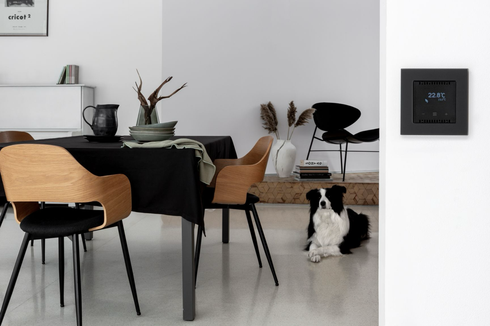 Polski system inteligentnego domu SIMON GO – czarny termostat na ścianie w nowoczesnym wnętrzu.