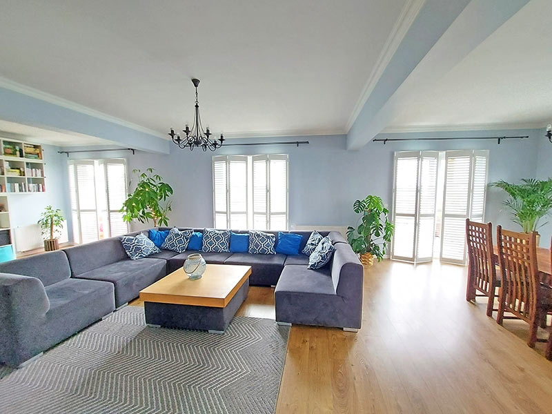 Salon z narożną sofą i białymi okiennicami shutters – eleganckie osłony okienne do wnętrz