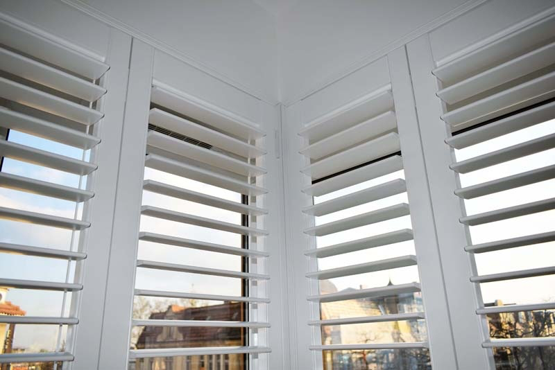 Białe okiennice shutters wewnętrzne – detal montażu w narożnym oknie