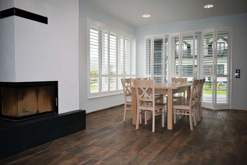 Jadalnia z kominkiem i białymi okiennicami shutters na dużych przeszkleniach
