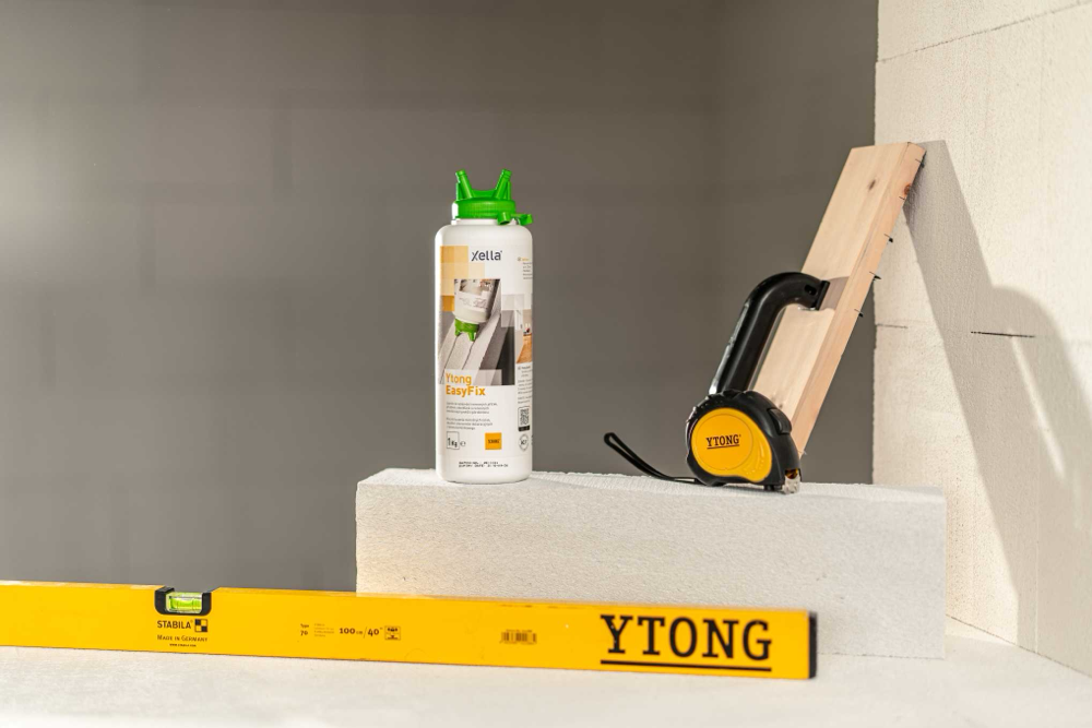 Klej do bloczków Ytong EasyFix na bloczku; w tle miarka Ytong i narzędzia do remontu