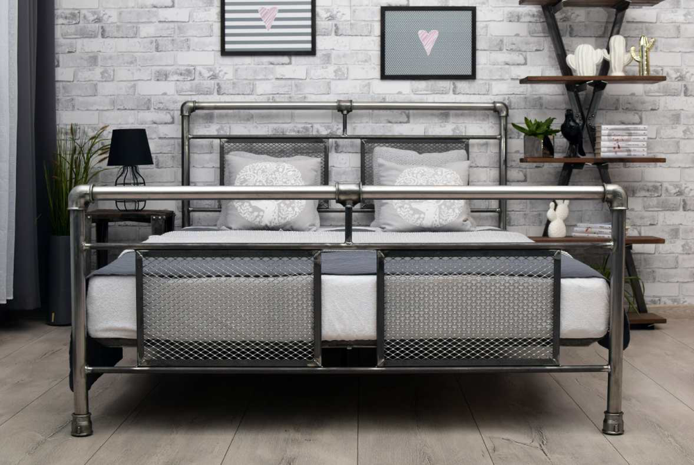 Metalowe łóżko industrialne z siatkowym wypełnieniem ramy na tle ściany z białej cegły.