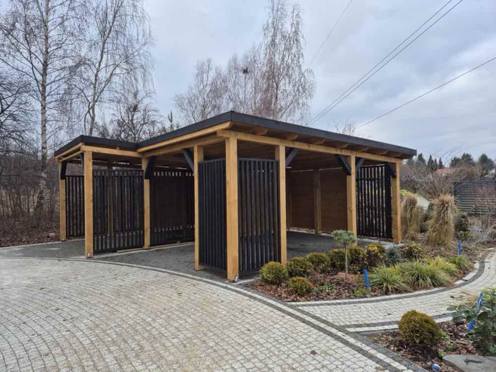 6. Podwójna wiata samochodowa Drewnotrik z drewnianą konstrukcją, czarnymi lamelami i dwoma zadaszonymi stanowiskami.