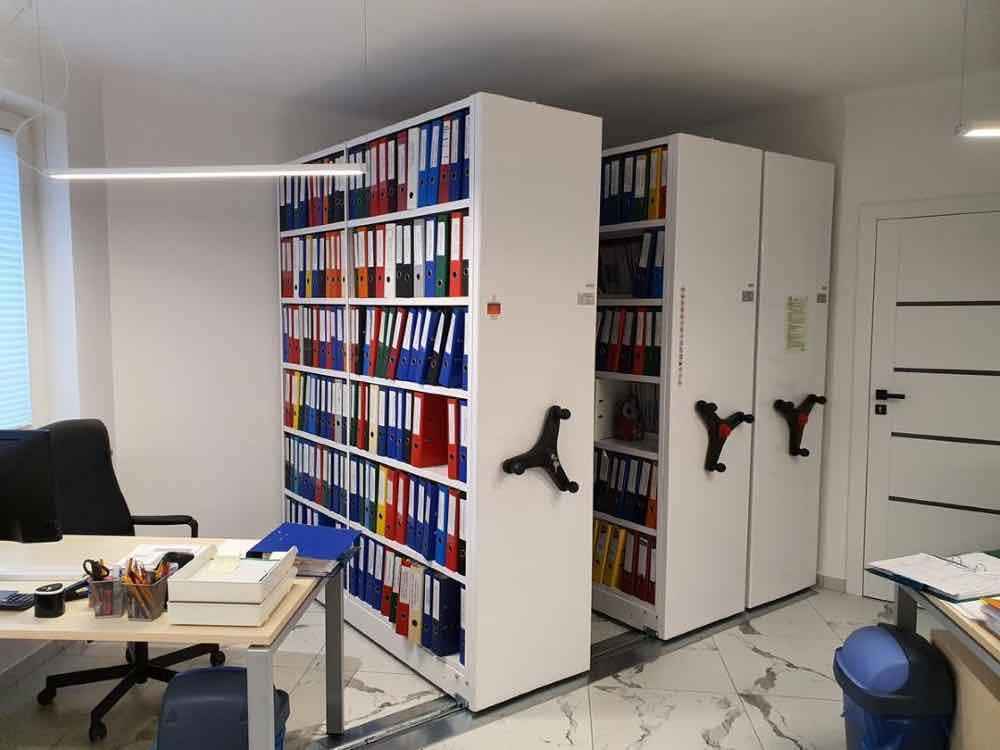 Regały przesuwne do archiwum z napędem mechanicznym w niewielkim biurze z dokumentacją w segregatorach