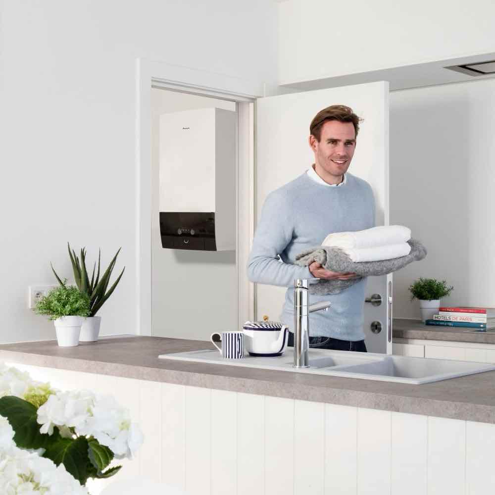 Jednostka wewnętrzna Daikin Altherma 3R w nowoczesnym domu, obok mężczyzna w błękitnym swetrze niosący koce i ręczniki.