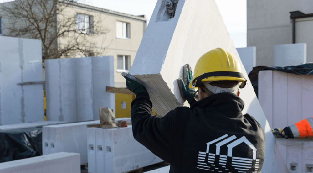 5. Pracownik w żółtym kasku prowadzi podnoszony przez dźwig wielkoformatowy panel z betonu komórkowego Ytong.