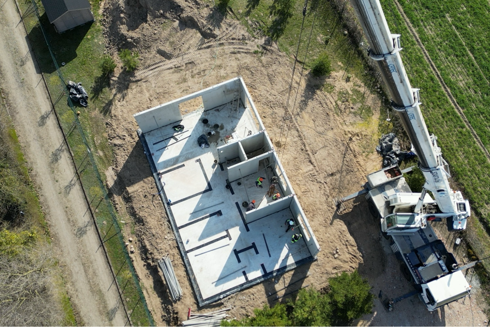 3. Widok z góry na montaż ścian domu prefabrykowanego z użyciem dźwigu.