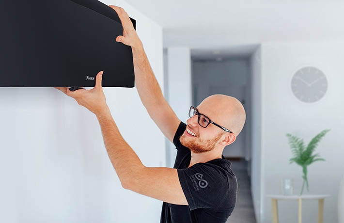 7. Instalator montujący czarną jednostkę wewnętrzną pompy ciepła Daikin na ścianie.